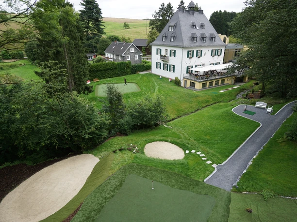 Short Game Area Eine historische Villa umgeben von grüner Landschaft und einem gepflegten Golfplatz mit Sandbunker.