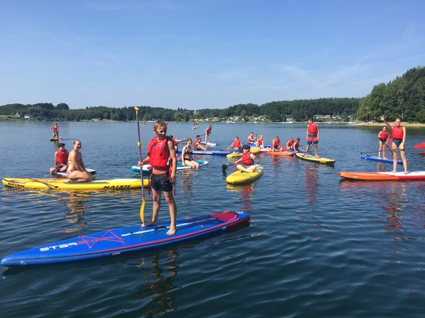 Stand-up-Paddling Gruppe von Menschen auf Stand-Up-Paddle-Boards auf einem ruhigen See unter blauem Himmel.