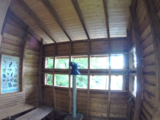 Vogelbeobachtungsstation an der Wupper Eine hölzerne Vogelbeobachtungshütte mit Fenstern, einem Fernglas auf einem Ständer und einer Bank.