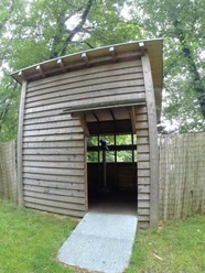 Vogelbeobachtungsstation an der Wupper Holzhütte mit schrägem Dach im Wald, offener Eingang auf grüner Wiese, Weg aus Metallplatten.
