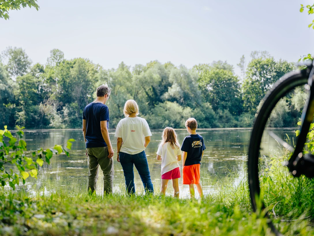 Haverkampsee_besimmazhiqi-99.jpg Eine Familie steht am bewachsenen Uferrand und blickt auf einen von Bäumen umgebenen See.