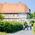 ehemaliges Jagdschloss Personen, darunter Kinder auf Fahrrädern, fahren eine Straße entlang vor einem ehemaligen Jagdschloss.