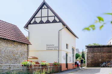 Historische Trafohausstation mit Fachwerkgiebel, umgeben von Blumenbeeten und Fahrrädern.