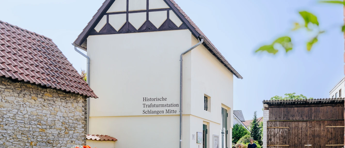 Historische Trafohausstation mit Fachwerkgiebel, umgeben von Blumenbeeten und Fahrrädern.