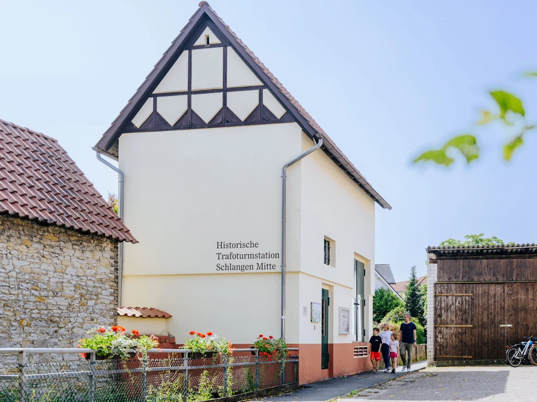 230626_besimmazhiqi-90.jpg Historische Trafohausstation mit Fachwerkgiebel, umgeben von Blumenbeeten und Fahrrädern.