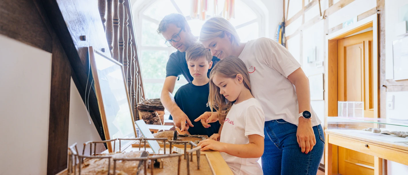 230626_besimmazhiqi-61.jpg Eine Familie betrachtet ein Miniaturmodell eines prähistorischen Hauses in einem hellen Museumsraum.