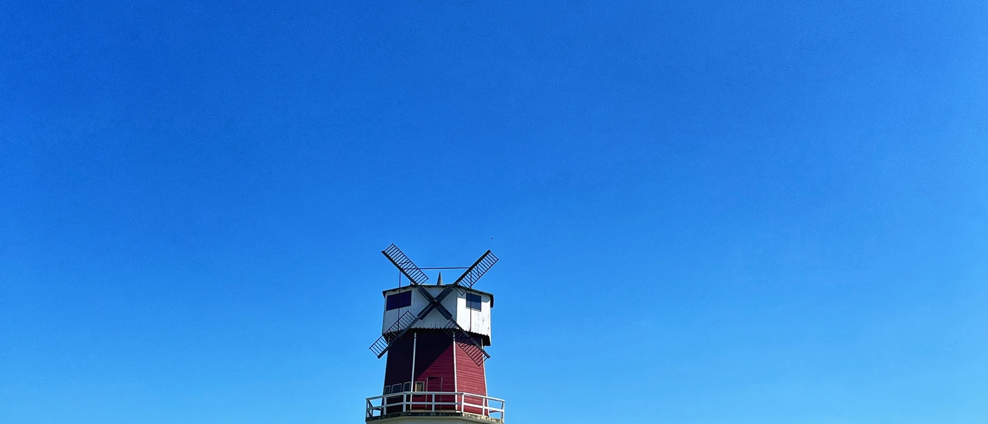 Eine rote Windmühle steht auf einem grünen Hügel unter einem strahlend blauen Himmel.