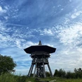 Ein hölzerner Aussichtsturm erhebt sich unter einem blauen Himmel mit verstreuten Wolkenformationen.