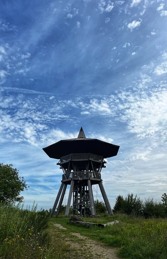 Foto Eggeturm.jpeg Ein hölzerner Aussichtsturm erhebt sich unter einem blauen Himmel mit verstreuten Wolkenformationen.