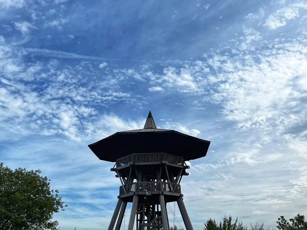 Foto Eggeturm.jpeg Ein hölzerner Aussichtsturm erhebt sich unter einem blauen Himmel mit verstreuten Wolkenformationen.