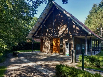 Foto Senne-Infozentrum.jpeg Holzgebäude des Senne-Infozentrums von Bäumen umgeben, blauer Himmel im Hintergrund.