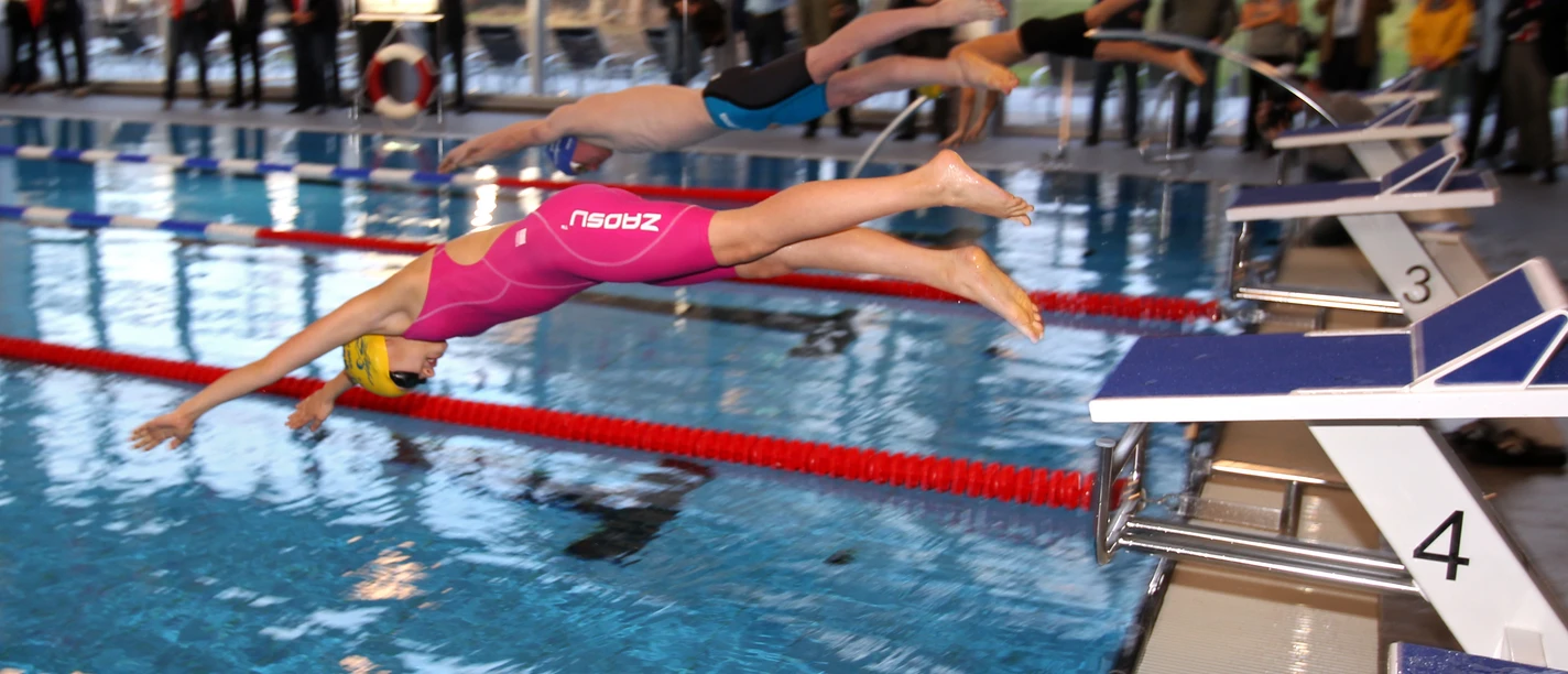 Wiehler Wasserwelt Mehrere Schwimmer starten gleichzeitig im Hallenbad von den Startblöcken für ein Wettkampfrennen.
