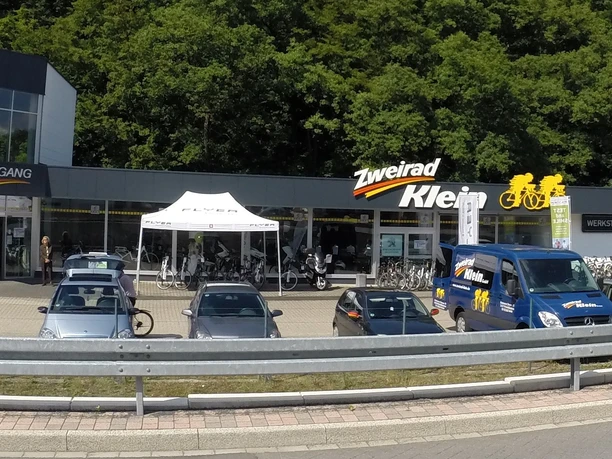 Zweirad Klein, Wiehl Bielstein Außenansicht eines Fahrradgeschäfts mit geparkten Autos, Firmenlogo und einem Lieferwagen im Vordergrund.