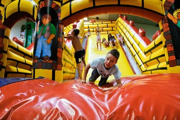 Tummel Dschungel Ein Kinderkletterparadies mit buntem Hüpfburg-Labyrinth, Kindern beim Klettern und Spielen.