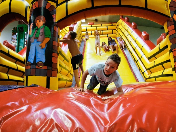 Tummel Dschungel Ein Kinderkletterparadies mit buntem Hüpfburg-Labyrinth, Kindern beim Klettern und Spielen.