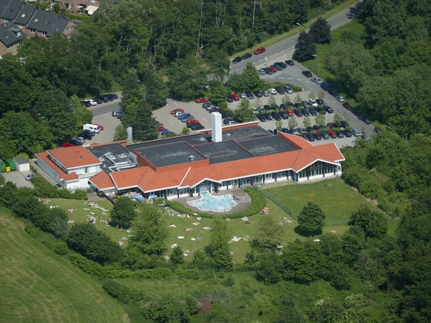 Burscheider Bad Luftaufnahme eines großen Gebäudes mit roten Dächern, Parkplätzen und umgebenden grünen Flächen.