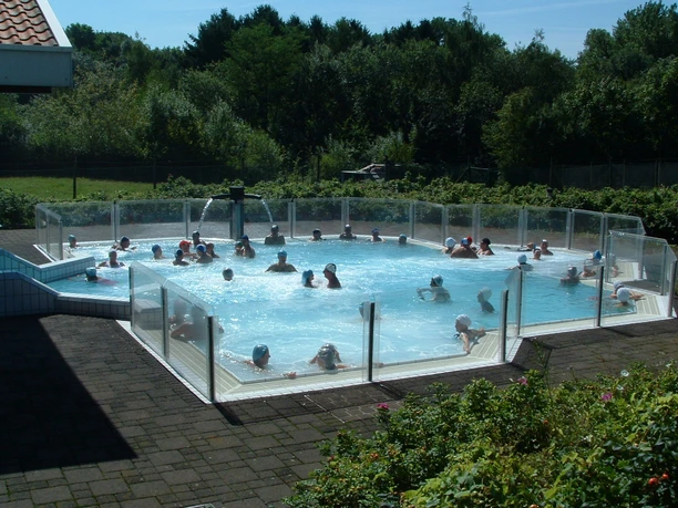 Burscheider Bad Menschen genießen ein sonniges Schwimmbad mit transparenten Schutzwänden, umgeben von Bäumen.