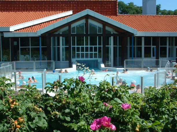 Burscheider Bad Menschen entspannen in einem Außenbecken mit gläsernem Gebäude im Hintergrund, umgeben von Blumen.