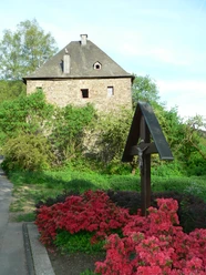Mediendatei Historisches, steinernes Gebäude im Grünen, umgeben von blühenden, roten Azaleensträuchern.