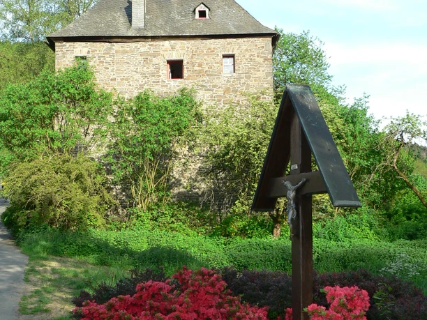 Mediendatei Historisches, steinernes Gebäude im Grünen, umgeben von blühenden, roten Azaleensträuchern.