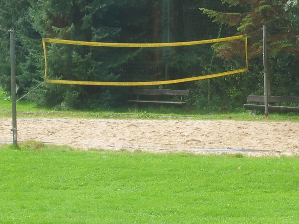 Volley-Bald Feld im Außenbereich Ein leerer Sand-Volleyballplatz mit Netz inmitten grüner Wiesen und umgeben von Bäumen.