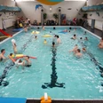 Dolphibad Morsbach Menschen schwimmen und spielen fröhlich in einem belebten Hallenbad mit Spielsachen im Wasser.