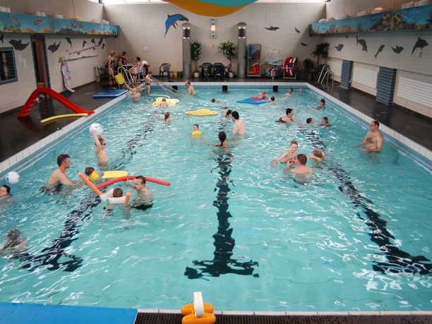 Dolphibad Morsbach Menschen schwimmen und spielen fröhlich in einem belebten Hallenbad mit Spielsachen im Wasser.