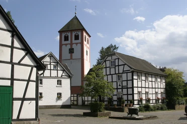 Odenthal Fachwerkhäuser umgeben eine Kirche mit Turm; ruhiger Platz, blaues Himmelsbild im Hintergrund.
