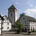 Odenthal Fachwerkhäuser umgeben eine Kirche mit Turm; ruhiger Platz, blaues Himmelsbild im Hintergrund.