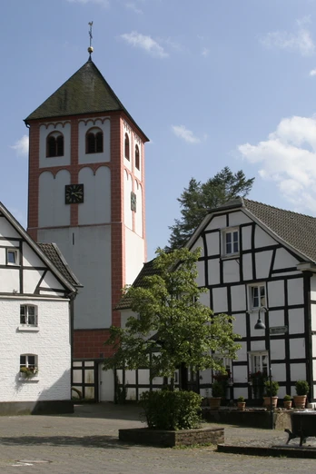 Odenthal Fachwerkhäuser umgeben eine Kirche mit Turm; ruhiger Platz, blaues Himmelsbild im Hintergrund.