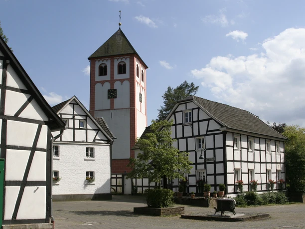 Odenthal Fachwerkhäuser umgeben eine Kirche mit Turm; ruhiger Platz, blaues Himmelsbild im Hintergrund.