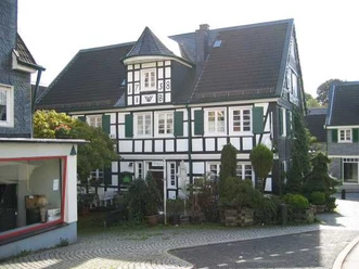 Mediendatei Fachwerkhaus mit grünen Fensterläden und Erkern in sonniger Dorfumgebung, Kopfsteinpflaster.