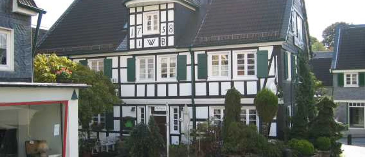 Mediendatei Fachwerkhaus mit grünen Fensterläden und Erkern in sonniger Dorfumgebung, Kopfsteinpflaster.