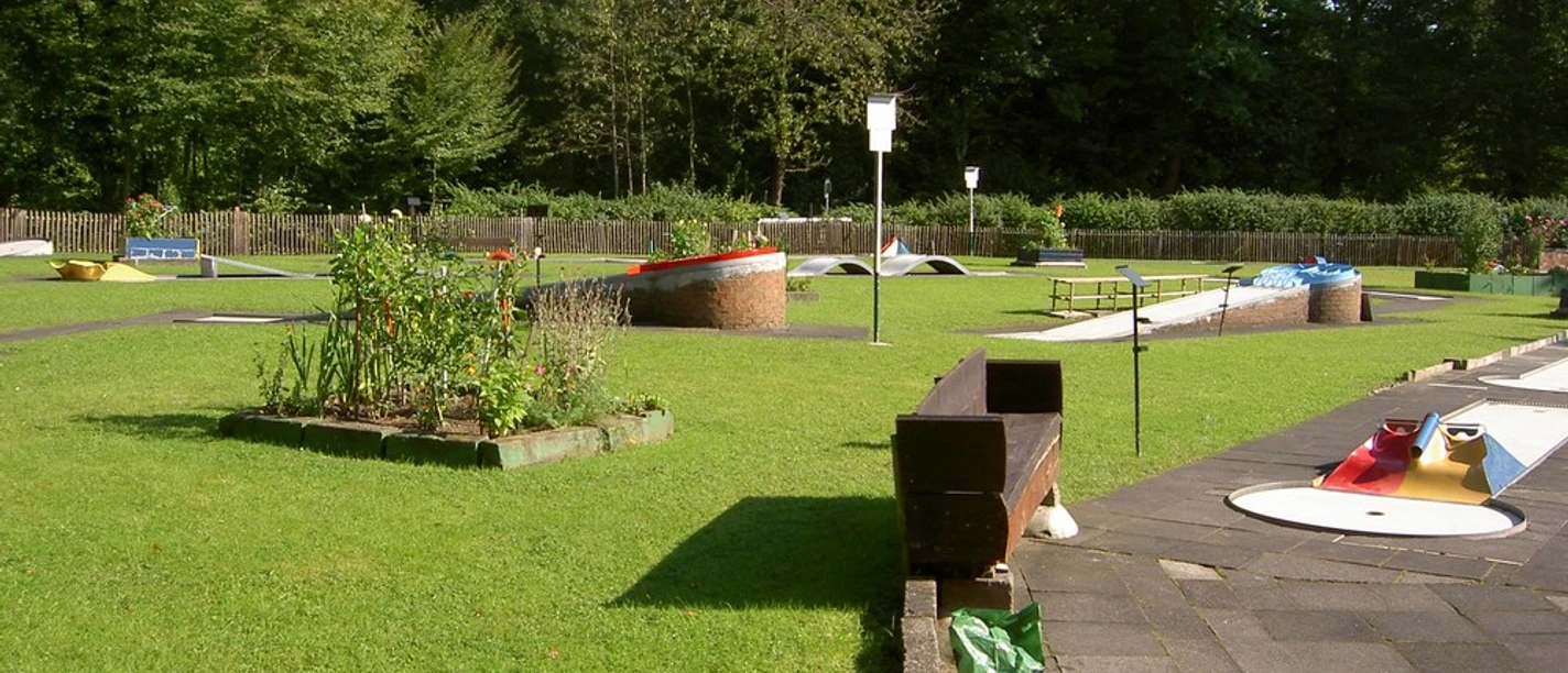 Minigolfanlage Paffrath Eine gepflegte Minigolfanlage mit verschiedenen Hindernissen, umgeben von grünem Rasen und Bäumen.