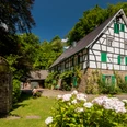 Lambertsmühle Fachwerkhaus im Grünen mit blühenden Hortensien und blauen Holzläden unter klarem Himmel.