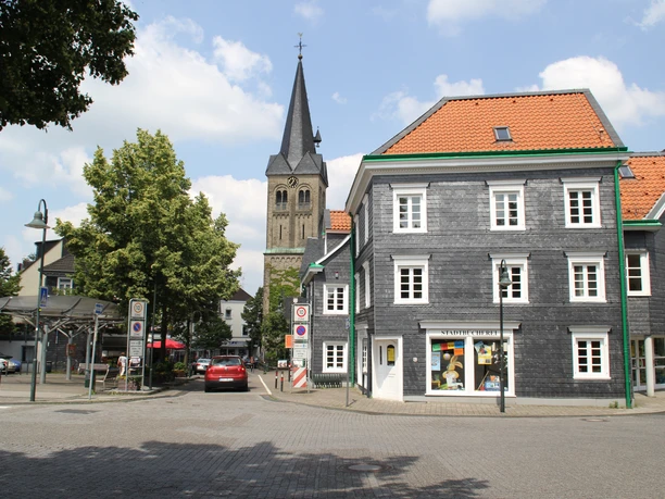 Ev. Kirche Burscheid Eine historische Kirche mit hohem Turm steht neben einem traditionellen Fachwerkhaus bei strahlendem Wetter.