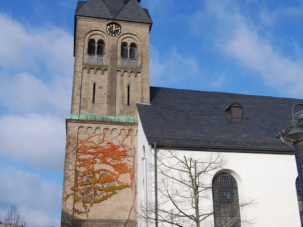 Ev. Kirche Burscheid Kirche mit hohem Turm, Uhr und Schieferdach. Wand mit Weinranken, blauer Himmel im Hintergrund.