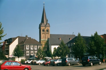 Ev. Kirche Burscheid Kirche mit markantem Turm umgeben von historischen Fachwerkhäusern auf einem sonnigen Platz.