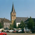 Ev. Kirche Burscheid Kirche mit markantem Turm umgeben von historischen Fachwerkhäusern auf einem sonnigen Platz.