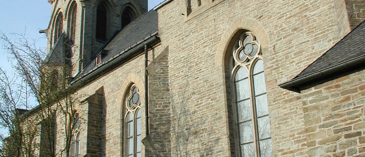 Mediendatei Seitenansicht einer alten, steinernen Kirche mit großen gotischen Fenstern und einem hohen Turm.