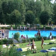 Waldfreibad Menschen genießen ein sommerliches Freibad, umgeben von Bäumen und Wiese, voller Entspannung.