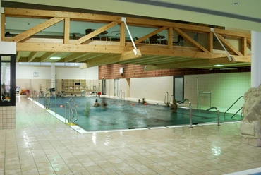 Badino Helles Hallenbad mit Holzträgern an der Decke, Menschen schwimmen in einem rechteckigen Pool.