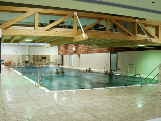 Badino Helles Hallenbad mit Holzträgern an der Decke, Menschen schwimmen in einem rechteckigen Pool.