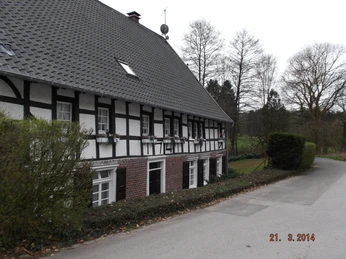 Grünscheider Mühle Fachwerkhaus mit schwarz-weißer Fassade an ruhiger Straße, umgeben von kahlen Bäumen im März.