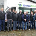 BürgerBus Verein Reichshof Elf Menschen posieren lächelnd vor einem Bürgerbus von Reichshof auf einem gepflasterten Platz.