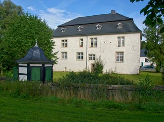 Denklinger Burg Ein historisches, zweigeschossiges Herrenhaus mit weißen Wänden und grauem Dach, umgeben von Grün.
