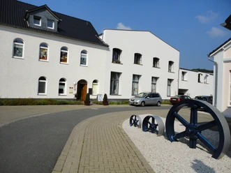 Ehemalige Werkhallen Klinkerweg führt zu zwei weißen Gebäuden mit Giebeldach, großen Fenstern und geparkten Autos.