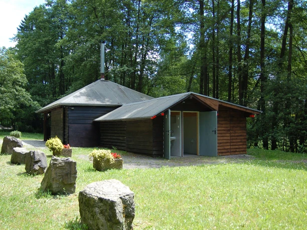 Grillhütte Windfus Holzhütte und benachbarte Sanitäranlage inmitten eines grünen Waldes mit grasbewachsenem Vorplatz.