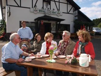 Bewirtung auf dem Pferdehof Hacke Eine Gruppe älterer Menschen sitzt an einem Holztisch vor einem Gasthof und genießt Kaffee.
