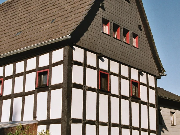 Haus Steeg, Vorderansicht Fachwerkhaus mit weißer Fassade und dunklen Holzbalken, steiles Dach, rote Fensterrahmen.